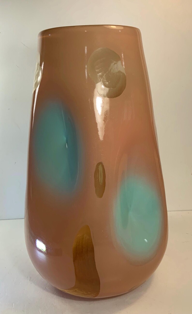 May include: A tall, teardrop-shaped glass vase in shades of peach and brown, with two large teal-colored spots and several smaller, lighter-colored spots. The vase has a glossy finish and a wide opening, suitable for floral arrangements.