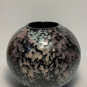 Puede incluir: Un jarrón decorativo redondo con un patrón moteado en negro, rosa y blanco. El jarrón tiene una abertura ancha y un acabado brillante. La forma general es esférica, y el diseño le da un aspecto artístico único.