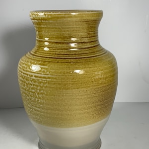 May include: A ceramic vase with a yellow and white glaze. The vase has a wide mouth and a narrow base. It is decorated with horizontal lines.