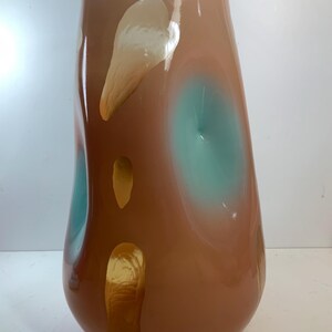 May include: A tall, decorative glass vase with a rounded base and a wide opening. The vase features a brown and peach color scheme with teal and gold accents. The design includes organic shapes and patterns.