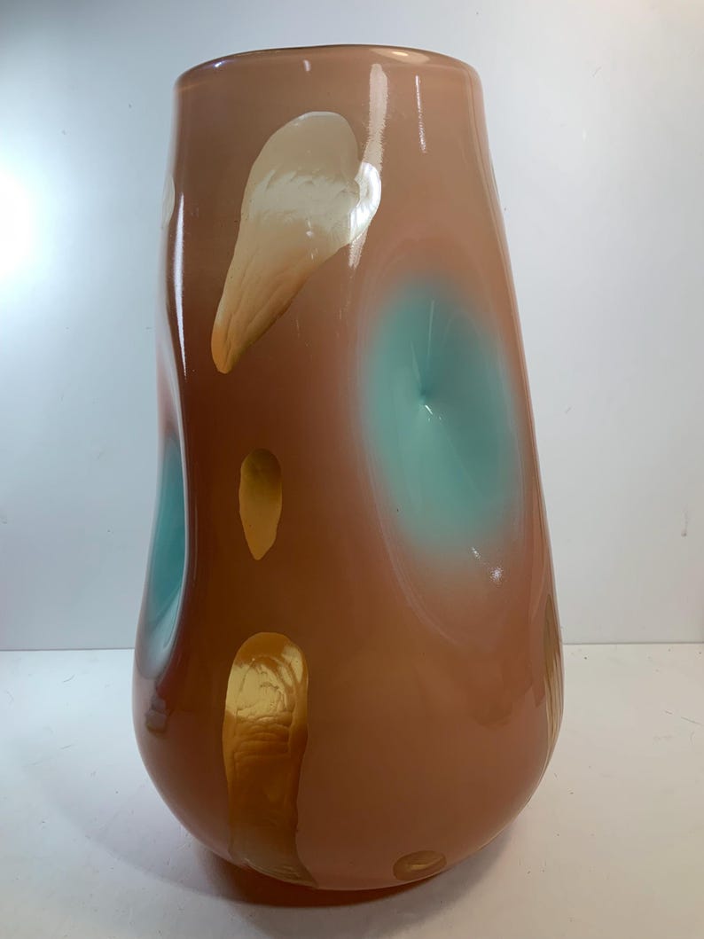 May include: A tall, decorative glass vase with a rounded base and a wide opening. The vase features a brown and peach color scheme with teal and gold accents. The design includes organic shapes and patterns.