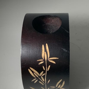 Puede incluir: Un jarr&oacute;n de madera marr&oacute;n oscuro con un dise&ntilde;o tallado de una planta con hojas y flores. El jarr&oacute;n tiene una abertura circular en la parte superior.