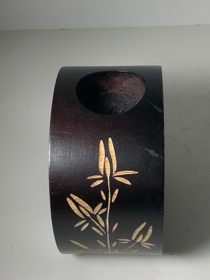 Puede incluir: Un jarr&oacute;n de madera marr&oacute;n oscuro con un dise&ntilde;o tallado de una planta con hojas y flores. El jarr&oacute;n tiene una abertura circular en la parte superior.