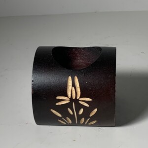 Puede incluir: Un anillo de madera marr&oacute;n oscuro con un dise&ntilde;o floral tallado. El anillo es hueco y podr&iacute;a usarse como un soporte decorativo.