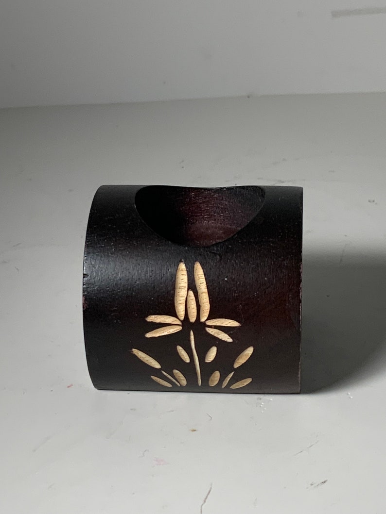 Puede incluir: Un anillo de madera marr&oacute;n oscuro con un dise&ntilde;o floral tallado. El anillo es hueco y podr&iacute;a usarse como un soporte decorativo.