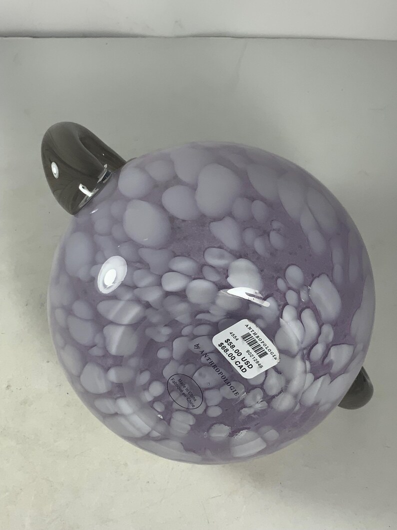 May include: A purple glass bowl with white speckles and a grey handle. The bowl is labelled "Anthropologie" and has a price tag of &pound;58.00 GBP and &pound;68.00 CAD.