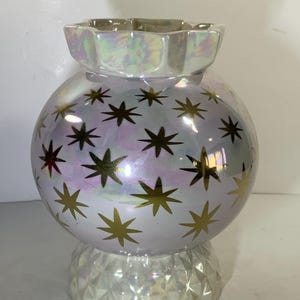 May include: Iridescent ceramic vase with a spherical body and a faceted base. The vase is decorated with gold starburst patterns. The top has a scalloped edge. The vase has a pearlescent finish that reflects multiple colors.