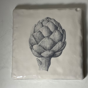 Puede incluir: Un azulejo de cerámica blanco con una ilustración en blanco y negro de una alcachofa.