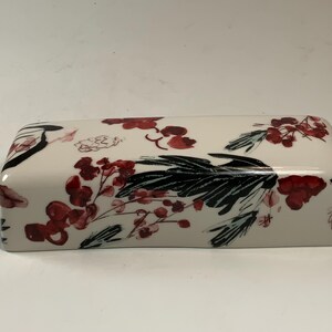 May include: Rectangular ceramic butter dish with a glossy finish. The dish is white with a floral design featuring red berries and black leaves. The design is repeated across the top and sides.