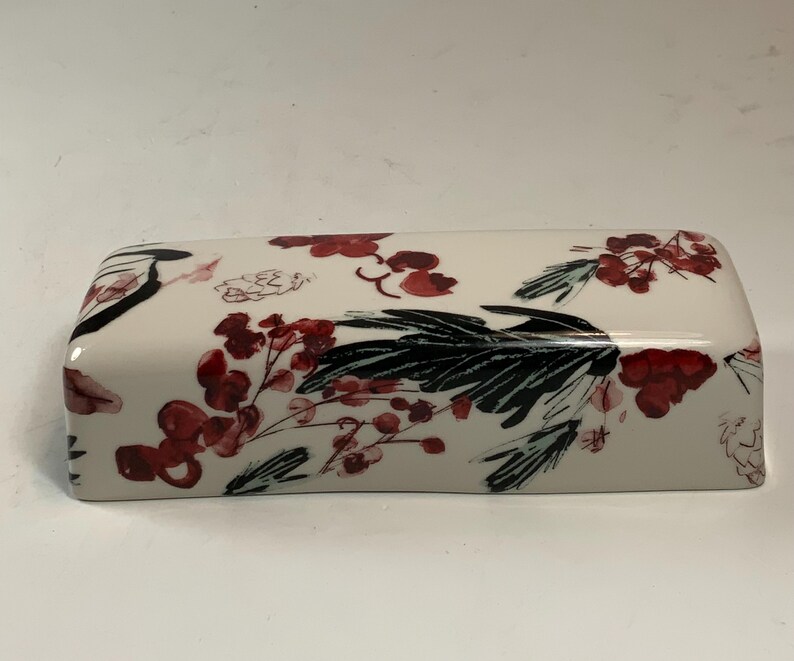 May include: Rectangular ceramic butter dish with a glossy finish. The dish is white with a floral design featuring red berries and black leaves. The design is repeated across the top and sides.