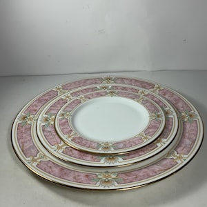 May include: Three pink and white porcelain dinner plates with gold trim and floral designs. The plates are stacked on top of each other.