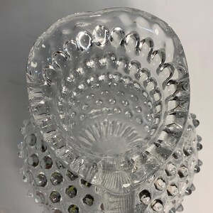 May include: Clear glass pitcher with a hobnail design. The pitcher has a scalloped rim and a handle. The hobnail pattern covers the body of the pitcher. The pitcher is empty and appears to be vintage.