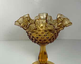 May include: A vintage amber glass candy dish with a ruffled rim and a textured, bubbled bowl. The dish sits on a pedestal with a round base.