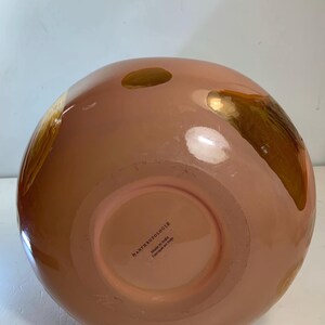May include: A peach-colored, round decorative vase with gold accents. The vase has a glossy finish and a wide opening. The bottom of the vase has a label that reads "by ANTHROPOLOGIE Made in India Fabriqu&eacute; en Inde."