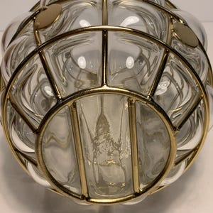 Op de afbeelding: Transparante glazen decoratieve kom met een goudkleurig metalen kooi-ontwerp. De kom heeft een ronde vorm met een reeks belachtige glazen secties. De goudkleurige metalen kooi voegt een vintage of retro esthetiek toe.