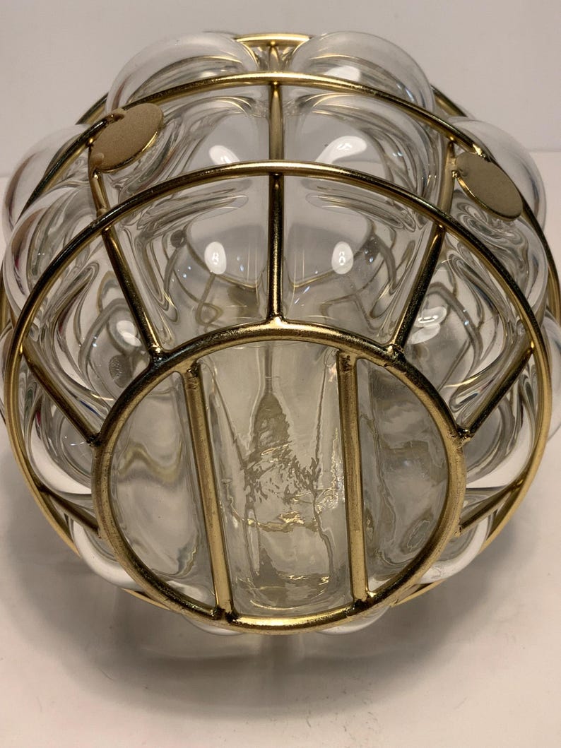 Op de afbeelding: Transparante glazen decoratieve kom met een goudkleurig metalen kooi-ontwerp. De kom heeft een ronde vorm met een reeks belachtige glazen secties. De goudkleurige metalen kooi voegt een vintage of retro esthetiek toe.