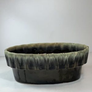 May include: A dark brown ceramic planter with a textured, ridged rim. The rim has a drip glaze effect with shades of green and tan. The oval-shaped planter is suitable for indoor or outdoor use.
