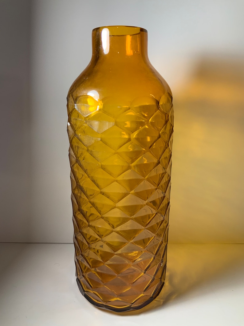 May include: A tall amber glass vase with a geometric diamond pattern.