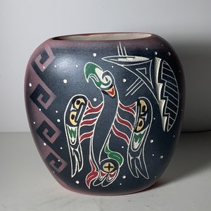 Op de afbeelding: Een donkergrijze keramische vaas met een gestileerd vogelontwerp in rood, groen, wit en zwart. De vaas heeft een afgeronde vorm en een getextureerd oppervlak.