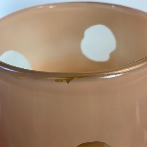 May include: A peach-colored glass vase with large white polka dots. The vase has a slightly flared rim and a smooth, glossy finish. The interior of the vase is a lighter shade of peach, creating a subtle gradient effect.