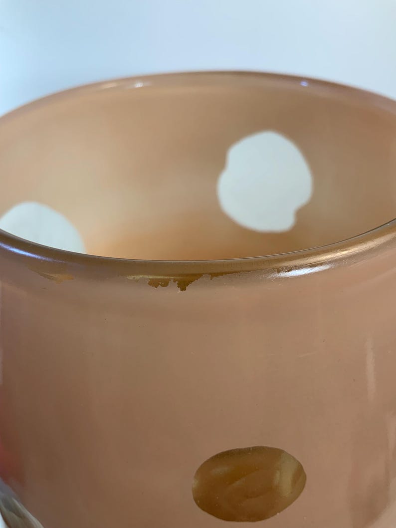 May include: A peach-colored glass vase with large white polka dots. The vase has a slightly flared rim and a smooth, glossy finish. The interior of the vase is a lighter shade of peach, creating a subtle gradient effect.