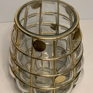 Op de afbeelding: Een heldere glazen vaas met een gouden metalen kooi-ontwerp. De vaas heeft een afgeronde vorm met een textuur, bubbelachtig patroon. De gouden kooi is gemaakt van verticale en horizontale staven, met kleine gouden schijfaccenten.