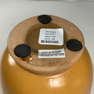 Pu&ograve; includere: Un'urna in ceramica marrone con un'etichetta che recita "terrain 34275677 CHALK URN $ 14.00" e "MADE IN VIETNAM FABRIQUE AU VIETNAM".