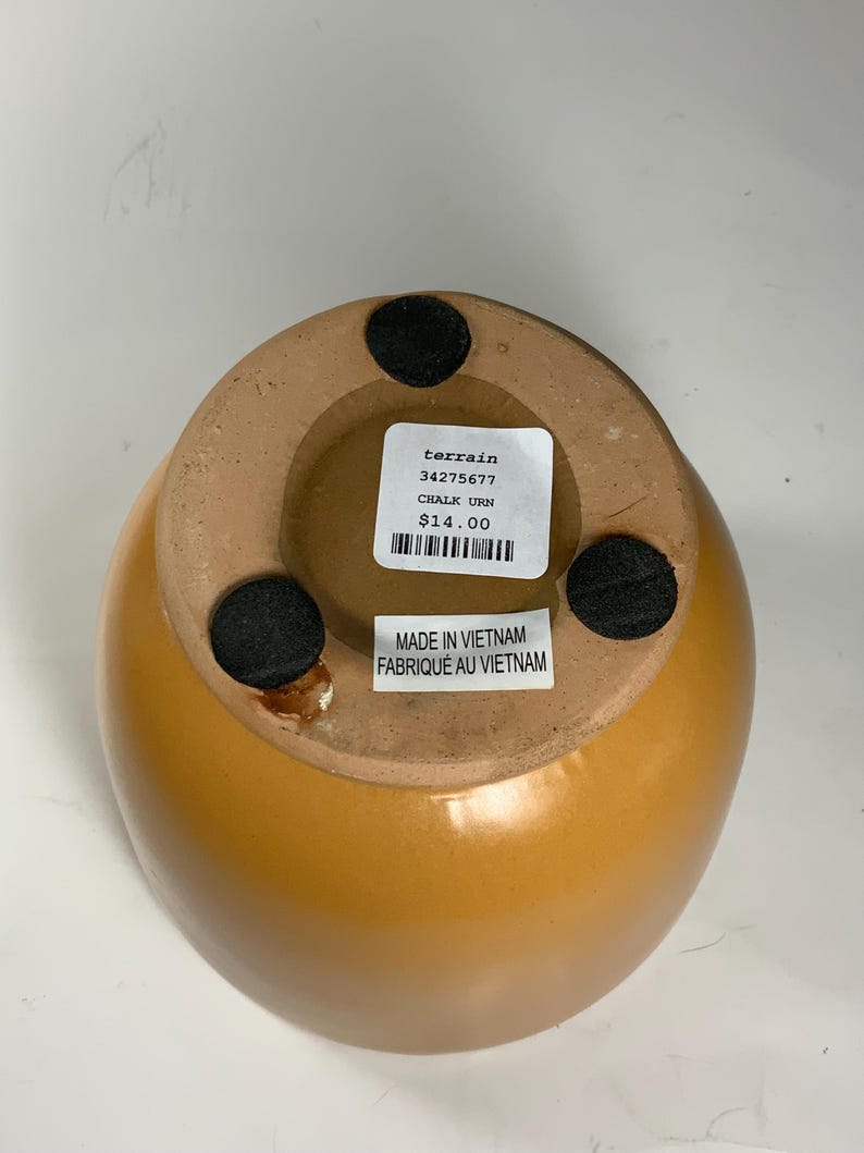 Pu&ograve; includere: Un'urna in ceramica gialla con un'etichetta in bianco e nero che recita "terrain 34275677 CHALK URN 14,00 &euro;" e "MADE IN VIETNAM FABRIQUE AU VIETNAM".