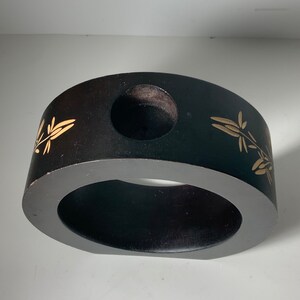 Puede incluir: Un anillo de madera negro con un dise&ntilde;o floral dorado y un agujero en el centro. El anillo tiene un di&aacute;metro de aproximadamente 25 cm.