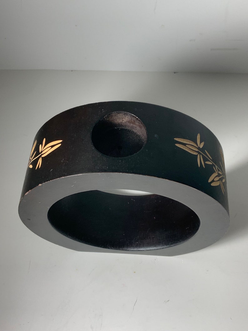 Puede incluir: Un anillo de madera negro con un dise&ntilde;o floral dorado y un agujero en el centro. El anillo tiene un di&aacute;metro de aproximadamente 25 cm.