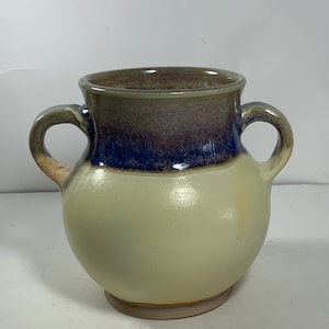 May include: A small, round, ceramic vase with two handles. The vase is glazed in shades of brown, blue, and cream.
