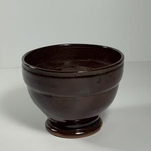 May include: A dark brown ceramic bowl with a wide rim and a pedestal base.