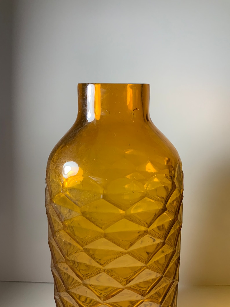 May include: An amber glass vase with a diamond pattern. The vase is empty and has a wide mouth.