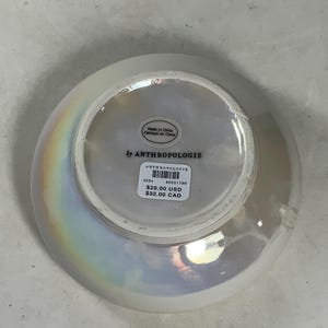 Może przedstawiać: Biała ceramiczna miska z iryzującym wykończeniem. Miska ma etykietę z napisem "by ANTHROPOLOGIE" i zawiera cenę: 28,00 USD i 32,00 CAD.