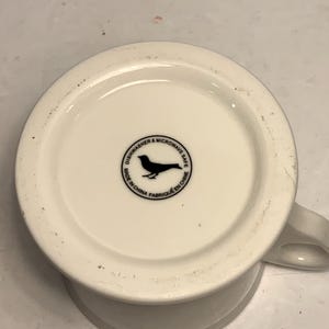 Puede incluir: Una taza de cer&aacute;mica blanca con asa negra y el texto "But First, Coffee" en estilo manuscrito. La taza est&aacute; sobre una superficie blanca. Ideal para bebidas calientes.