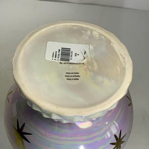 May include: A pearlescent vase with a light purple and gold star design. The vase has a wide opening and a slightly ruffled rim. The label reads "by Anthropologie".