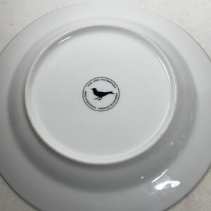 May include: White ceramic plate with a black bird logo on the bottom. The logo reads "Hand Wash Recommended, Made in Indonesia, Fabrique en Indonesie".