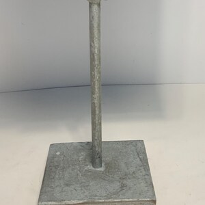 May include: A metal display stand with a square base and a vertical support. The stand is made of a silver-colored metal. The base is a square shape, and the vertical support is a cylindrical rod.