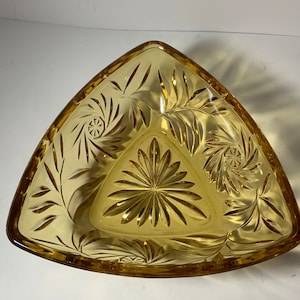 Op de afbeelding: Een driehoekige amber glazen schaal met een decoratief geëtst patroon. De schaal heeft een swirl-ontwerp in het midden en een bladpatroon rond de randen.
