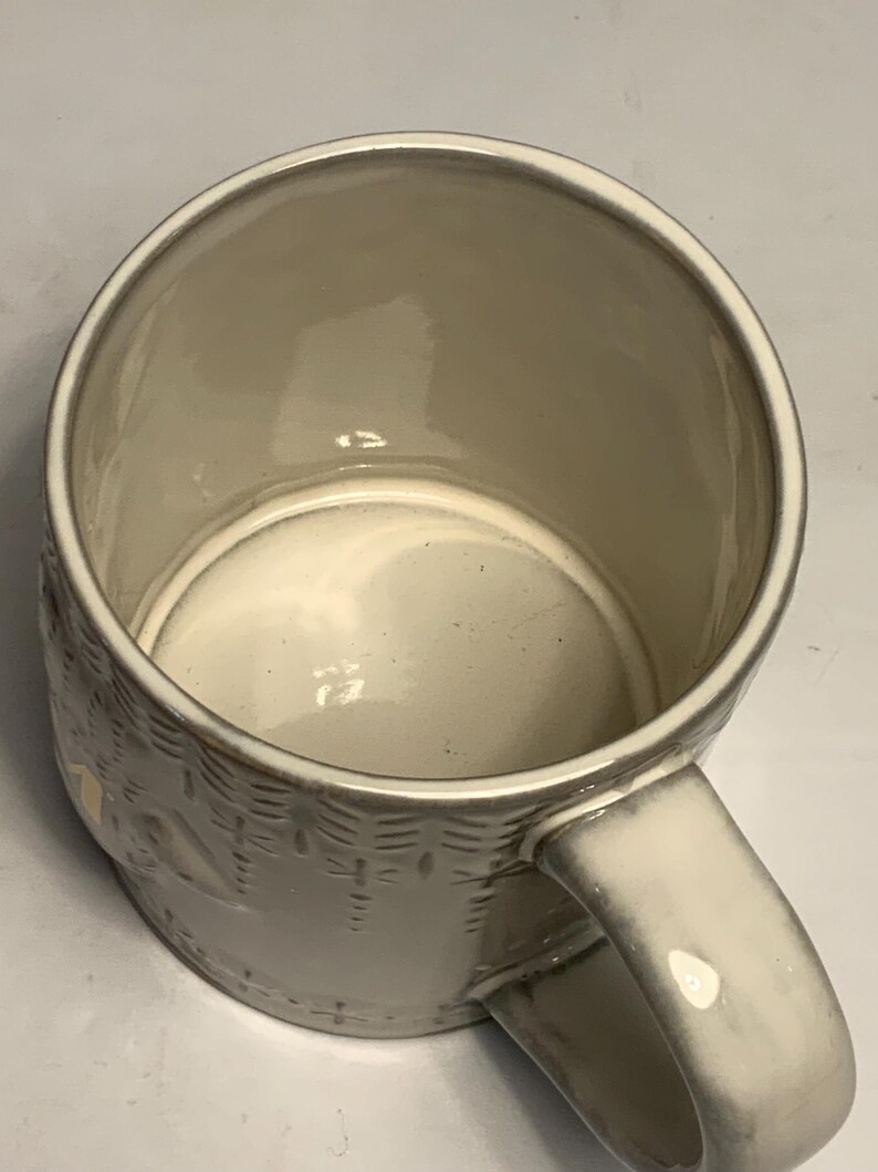 May include: A cream-colored ceramic mug with a textured basket weave design. The mug has a rounded handle and a smooth, glossy interior. The mug is empty and appears to be clean.