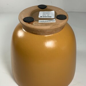 Pu&ograve; includere: Un vaso in ceramica color terracotta con corpo rotondo e un'ampia apertura. Il vaso ha un'etichetta sul fondo che recita "Terrain 34275677 Chalk Urn 14,00 &euro;" e "Made in Vietnam".