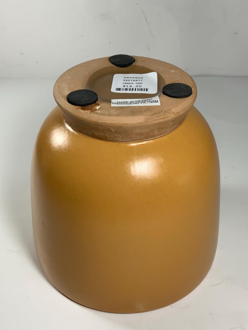 Pu&ograve; includere: Un vaso in ceramica color terracotta con corpo rotondo e un'ampia apertura. Il vaso ha un'etichetta sul fondo che recita "Terrain 34275677 Chalk Urn 14,00 &euro;" e "Made in Vietnam".