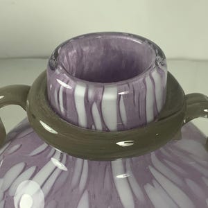 May include: A purple glass vase with white swirls and dots. The vase has a wide mouth and two handles.