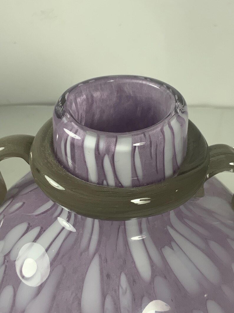 May include: A purple glass vase with white swirls and dots. The vase has a wide mouth and two handles.