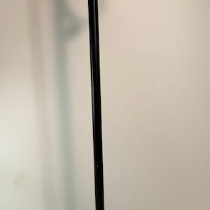 Puede incluir: Un perchero de metal negro con un adorno decorativo en la parte superior. El perchero tiene un gancho curvo para colgar objetos y una base redonda para mayor estabilidad. El perchero mide aproximadamente 152 cm de alto.