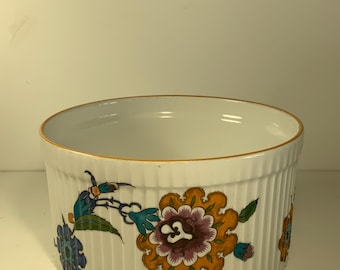 Op de afbeelding: Witte keramische kom met een geribbelde buitenkant en een gouden rand. De kom is versierd met kleurrijke bloempatronen in tinten oranje, paars, blauw en groen. De kom heeft een ronde vorm.