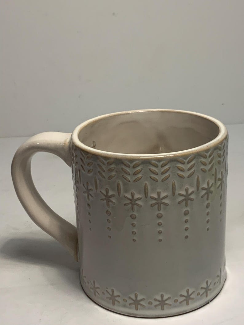Peut inclure: Mug en c&eacute;ramique gris clair avec une anse cr&egrave;me. Le mug pr&eacute;sente un motif en relief de flocons de neige et de motifs de feuilles. L'int&eacute;rieur est beige clair. Un design simple et &eacute;l&eacute;gant pour un usage quotidien. Id&eacute;al pour les boissons chaudes ou froides.