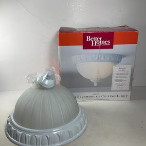 May include: A white ceiling light fixture with a frosted glass shade and decorative trim. The box says "Better Homes and Gardens" and "Flushmount Ceiling Light".