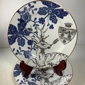 May include: Two white ceramic plates with a blue and gold floral design and a black and white deer illustration. The plates have a gold rim.