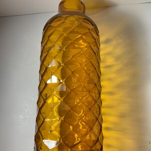 May include: A tall, amber glass vase with a diamond-shaped pattern. The vase is empty and has a rounded bottom.